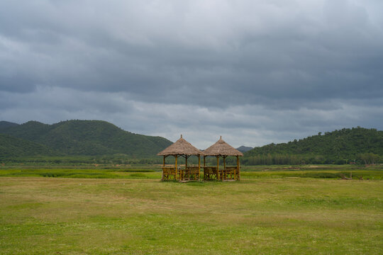 Two bamboo thatched pavilions on a grass field under stormy clouds
