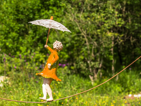 Whimsical Garden Statue Balancing on Tightrope Holding Lace Umbrella in Sunny Green Park