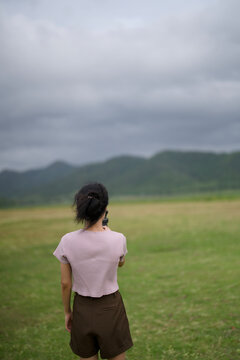 Rear view of a woman standing alone in a green field under grey clouds