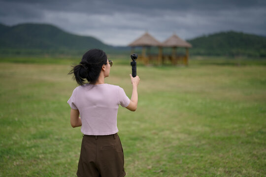 Woman filming bamboo pavilions across an open field with a gimbal