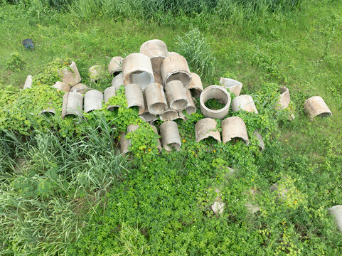 A pile of discarded concrete culverts covered in weeds