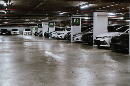 Indoor parking garage with rows of parked cars, concrete floor, overhead lighting, and clear B2 parking signs in a modern commercial building.
