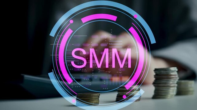 Hands are seen on a calculator while coins are arranged on a desk. The SMM logo is displayed in front of the scene. This shows planning for social media marketing efforts.
