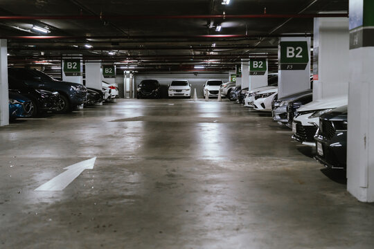 Indoor parking garage with rows of parked cars, concrete floor, overhead lighting, and clear B2 parking signs in a modern commercial building.
