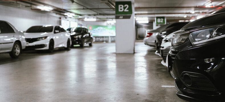 Indoor parking garage with rows of parked cars, concrete floor, overhead lighting, and clear B2 parking signs in a modern commercial building.