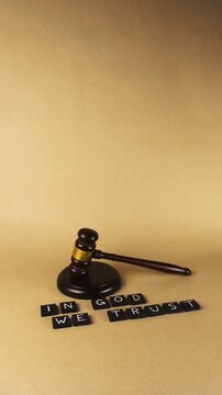 Wooden judge gavel resting beside the national motto of the United States, In God We Trust, spelled out in letter tiles, conceptualizing the intersection of faith, law, and justice