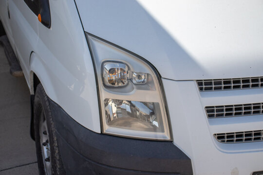 Close-up of a white commercial van headlight and front grille. Concept of delivery transport, commercial vehicles, auto optics, and fleet logistics.