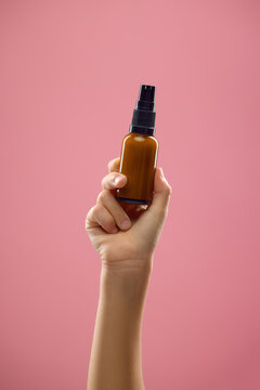 Hand holding brown cosmetic pump bottle on soft pink background. Concept of premium cosmetic branding, beauty serum advertising, and facial skincare.