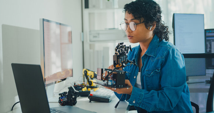 Young African American female robotics engineer discussing mechanical part on video call in laboratory. Remote work, virtual training, online meeting, future technology, technical support concept.