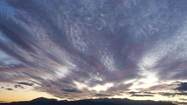 日没でシルエットの山陰とオレンジ色、紫色、青色にグラデーションの空とうろこ状の雲が奥から手前にゆっくり流れる様子のタイムラプス