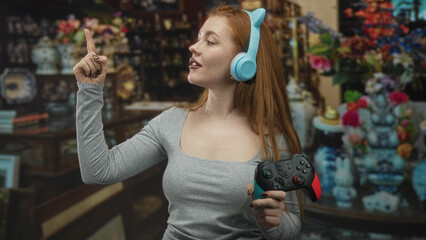 Woman holding gamepad and wearing cat ear headphones points index finger in building  playful gaming fun. © Krakenimages.com