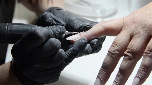 Manicurist uses a ball drill bit to treat the cuticle area during professional hardware manicure. Close-up nail care procedure in a beauty salon.