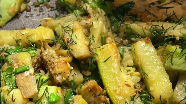 Person stirs homemade fried zucchini with fresh herbs in a frying pan, healthy vegetable dish, keto cooking, low carb meal.