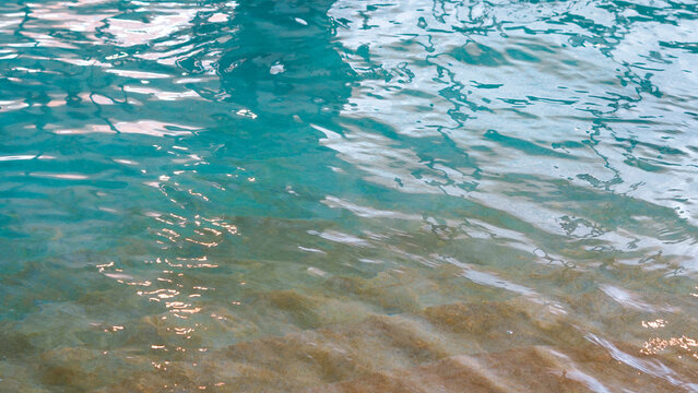 Gentle ripples and reflections shimmer across the surface of a swimming pool near its tiled edge