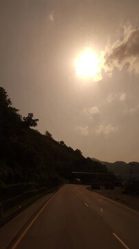 Scenic road footage showing the warm evening sun over lush forested hills along the route from the Manakamana Temple area toward Kathmandu, Nepal. The video captures a peaceful mountain landscape