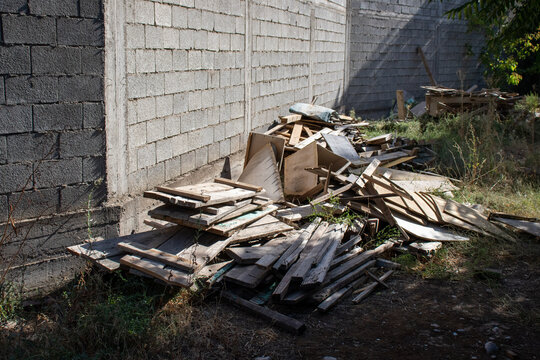 A pile of scrap wood and construction debris dumped near a cinder block wall outdoors. Concept of renovation waste, building site cleanup, and waste management.