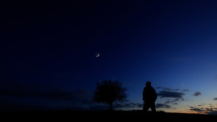 Silhouette of a person in nature observing night sky, Moon, stars and planets from a remote location. © astrosystem