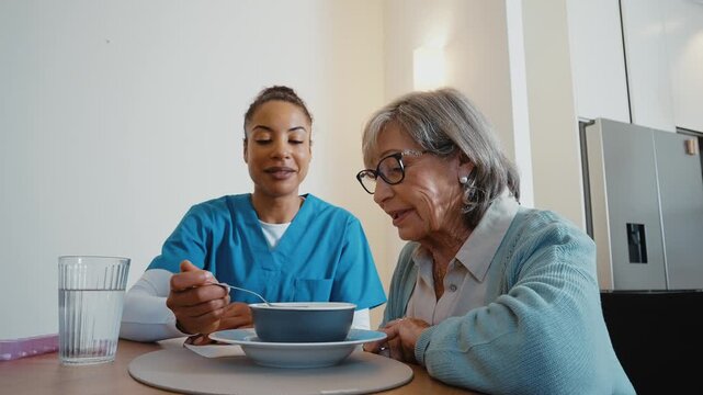 Kind caregiver feeding a senior woman with soup during mealtime at a retirement home. Helpful young nurse providing support and assistance to an older patient. Ensuring her nutritional needs are met