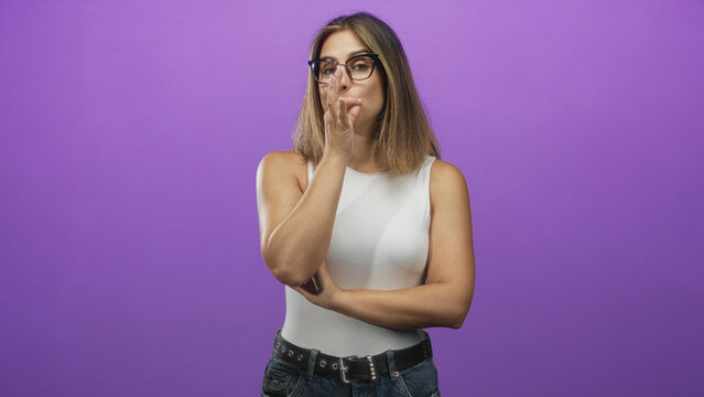 Woman with fingers at lips blowing kiss gesture in studio with purple backdrop and sleeveless white bodysuit; playful confidence.