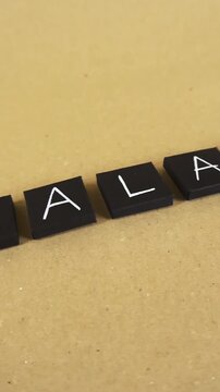 Smooth camera movement over black squares with white letters spelling out the word halal, representing Islamic dietary law and permissible food products on a simple brown cardboard background