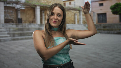 Young brunette woman with bare arms presenting palms as if holding an invisible object, posing in a stone plaza in front of a building  curiosity. © Krakenimages.com