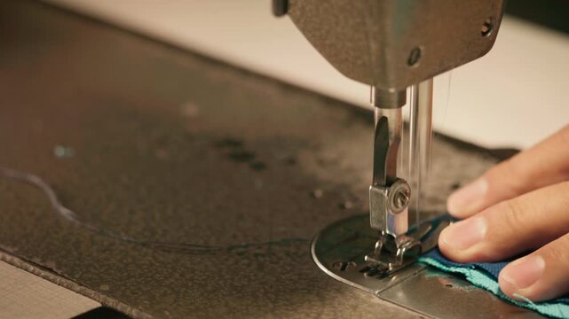 Close-up footage of an industrial single-needle lockstitch sewing machine forming stitches on blue fabric, highlighting handmade craftsmanship and textile production.