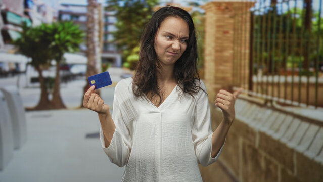 Woman holding creditcard in hand, palm raised dismissive gesture while turning away on a street; payment frustration.