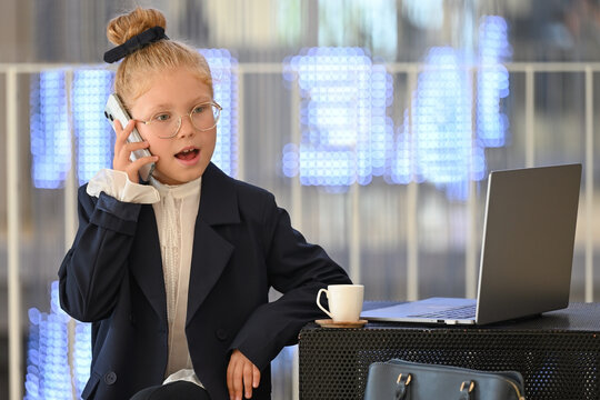An expressive girl in a business suit and glasses is talking on her smartphone.