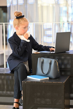A little girl is working on a laptop, sipping coffee.