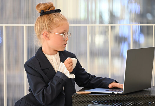 A little girl is working intently at a modern desk with a cup of coffee.