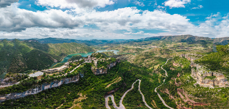 Aerial panoramic view of Siurana village perched on dramatic cliffs above winding mountain roads and Siurana Reservoir in Catalonia, Spain.