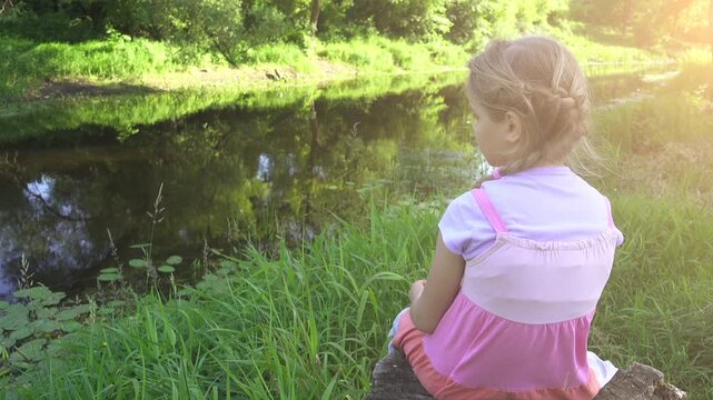 Little sad girl sits on shore of small river