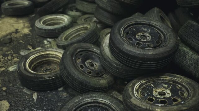 Foregroundfocused tires with shallow depth of field highlighting worn treads and rims, soft background stacks suggest larger pile, cinematic framing useful