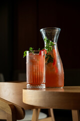 Drink and pitcher sit on a wooden table in a dimly lit space with chairs around © Tkachenko Alexey