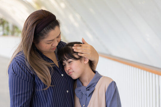 asian middle aged single mother comforting her sad and crying primary school daughter in sunny outdoor scene, motherly love and support