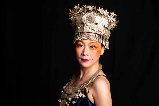 A portrait of an oriental woman wearing ornate Miao silver jewelry against a black background.