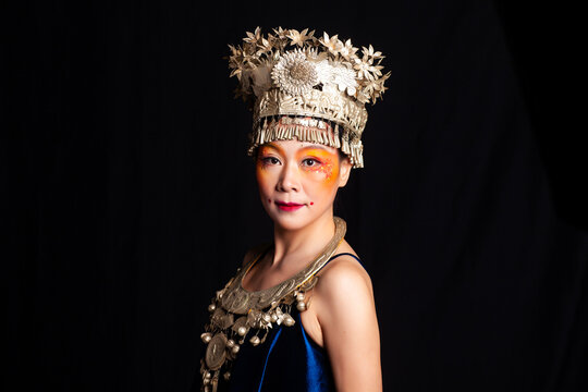 A portrait of an oriental woman wearing ornate Miao silver jewelry against a black background.