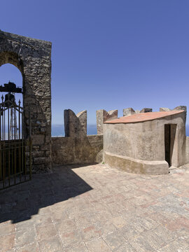Observation deck on King Frederick's Tower in Erice, Sicily, showing the stone bell archway, swallowtail merlons, and a blue sea background.