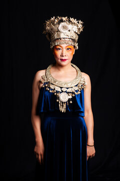 A portrait of an oriental woman wearing ornate Miao silver jewelry against a black background.
