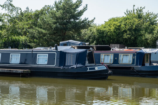 Dark blue narrowboat moored beside other traditional canal boats on a quiet English inland waterway.