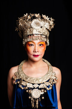 A portrait of an oriental woman wearing ornate Miao silver jewelry against a black background.