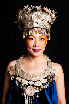 A portrait of an oriental woman wearing ornate Miao silver jewelry against a black background.