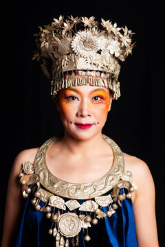A portrait of an oriental woman wearing ornate Miao silver jewelry against a black background.