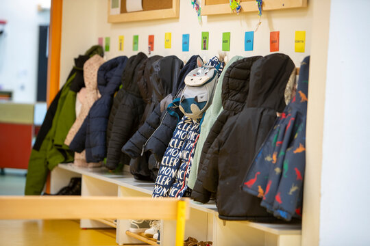 Le vestiaire d'une &eacute;cole ou d'une garderie avec plusieurs manteaux d'enfants suspendus &agrave; des pat&egrave;res au-dessus d'un banc, surmont&eacute; d'&eacute;tiquettes nominatives color&eacute;es.