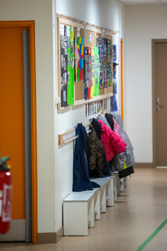 Un couloir d'&eacute;cole maternelle avec un espace de vestiaire, des pat&egrave;res fix&eacute;es au mur, des bancs de rangement blancs et des panneaux d'affichage d'activit&eacute;s d'enfants.