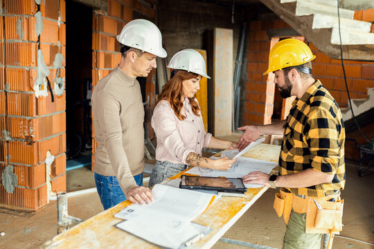 Contractor explaining blueprints to clients on construction site.