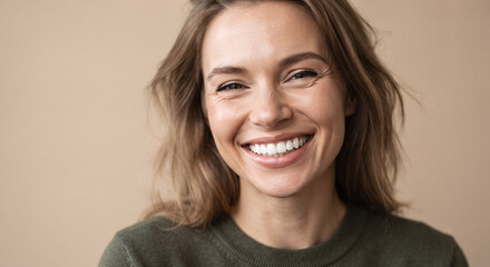 Naklejka premium Portrait of genuinely smiling young woman with beautiful white teeth on beige background