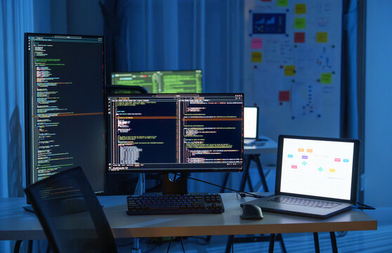 Software development office Workstation setup with multiple monitors displaying code and development diagrams during a nighttime coding session