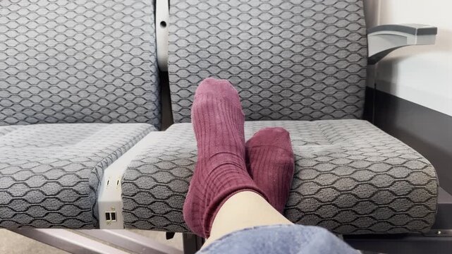 Feet in burgundy socks resting on the opposite seat inside a commuter train, illustrating a violation of public transport etiquette. Casual everyday scene, urban travel, and disregard for shared-space