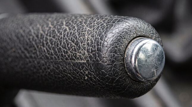 Macro close-up of a worn black textured automotive handbrake lever with a scratched chrome button